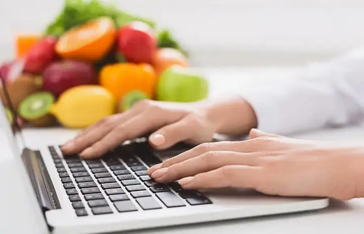 Hands on keyboard with fruits and vegetables in the background